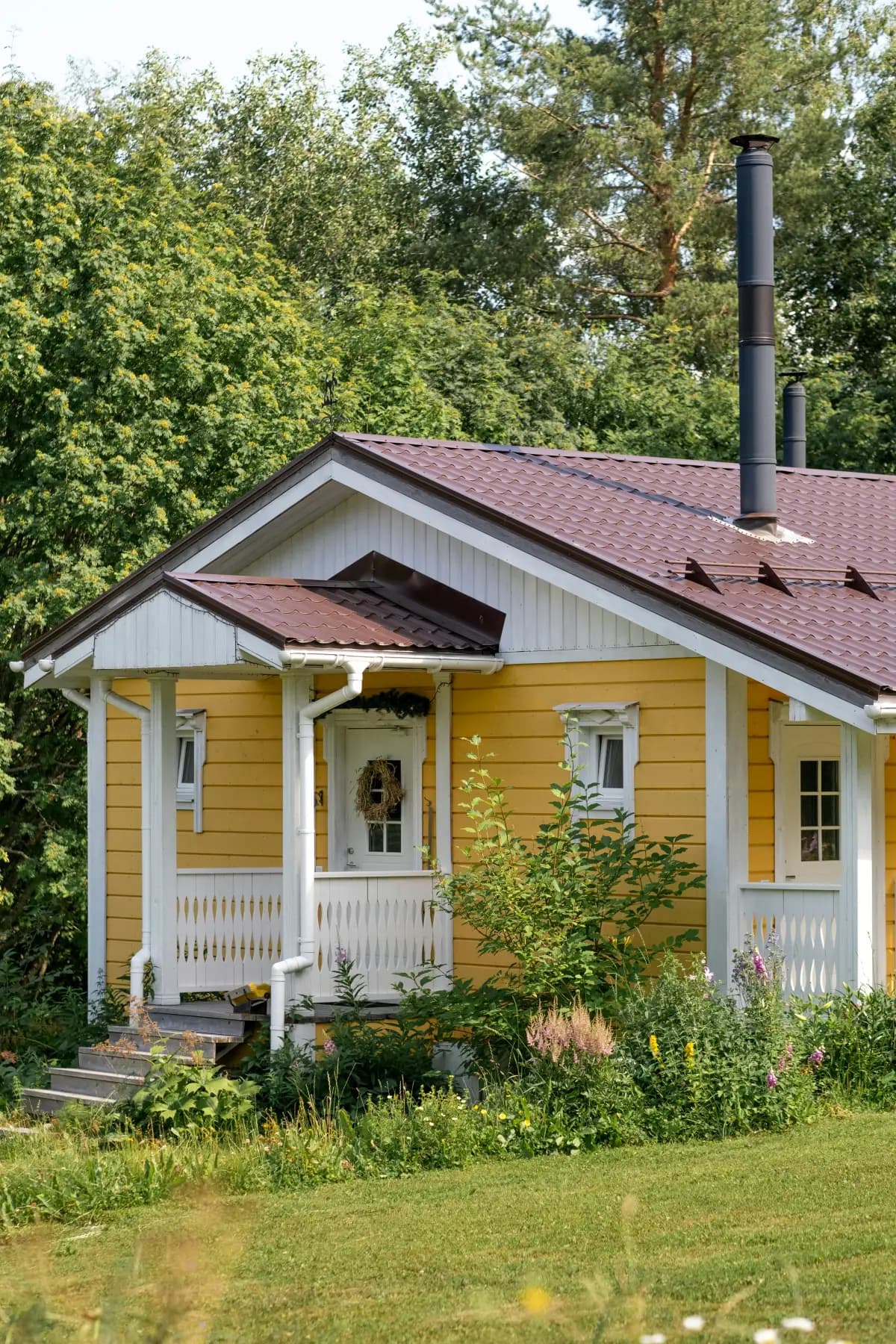 Gult trehus med veranda og frodig hage omkranset av trær