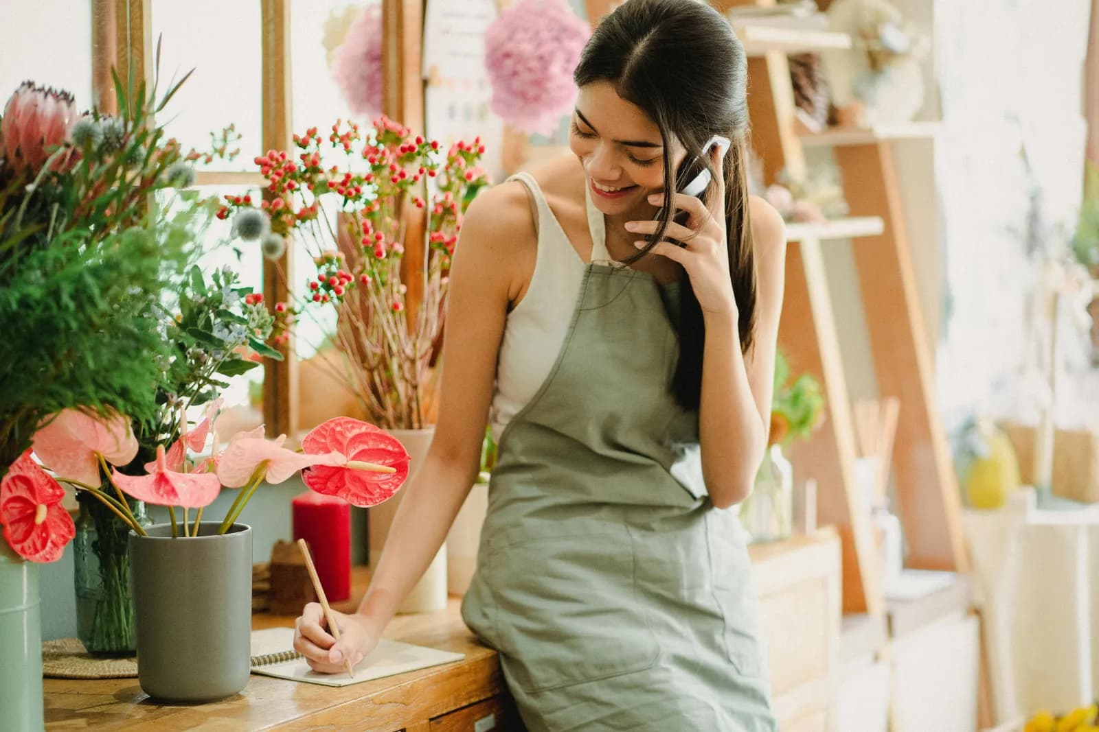 Blomsterhandler noterer mens hun snakker i telefonen i butikken