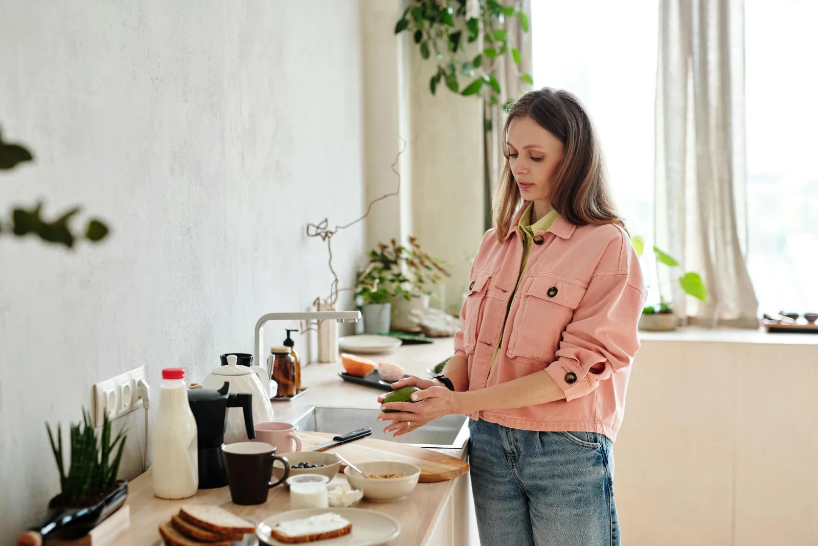 Kvinne ved kjøkkenbenken med frokost og planter i dagslys