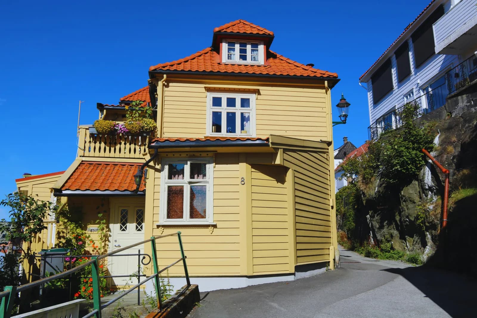 Gult trehus med rødt tegltak i en bratt gate under blå himmel